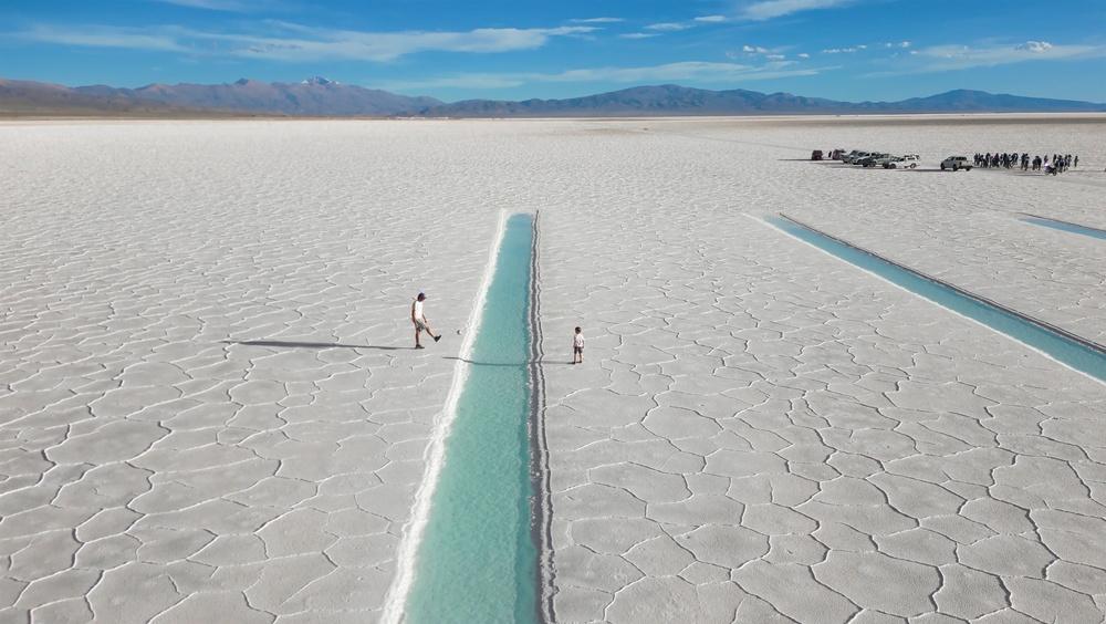 Father and son playing soccer next to turquoise saltwater pools in the white salt flats of Salinas Grandes, Argentina