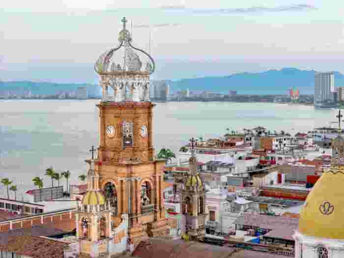 Historic church tower and rooftops along the Malecón in Puerto Vallarta overlooking the ocean and distant mountains.