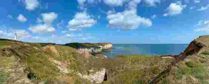 image Panoramic view of the Yorkshire Coast chalk cliffs and a white lighthouse overlooking the North Sea under a bright blue sky.