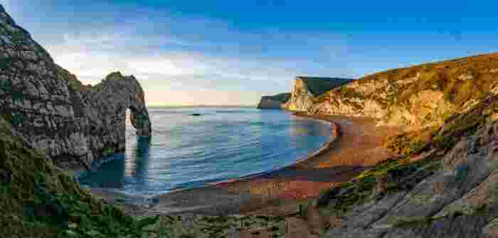 image Panoramic view of Durdle Door natural limestone arch on the Jurassic Coast in Dorset, with a pebble beach and calm blue sea.