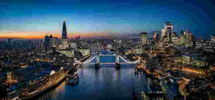 image Aerial panoramic view of London at dusk featuring the illuminated Tower Bridge and the Shard skyscraper reflecting over the River Thames.