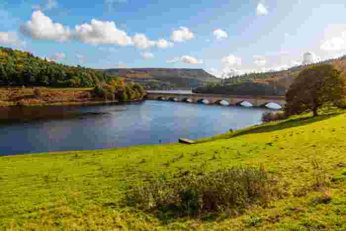 image Ladybower Reservoir in the Peak District with a stone arched viaduct crossing the water, framed by autumn woodland and moorland hills.