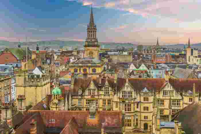 image Rooftop panoramic view of Oxford's historic skyline featuring medieval stone buildings, church spires, and terracotta rooftops at dusk.