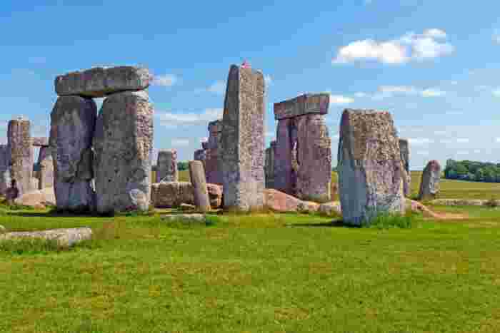 image Ancient Stonehenge megalithic stone circle standing on a green meadow under a bright blue sky in Wiltshire, England.