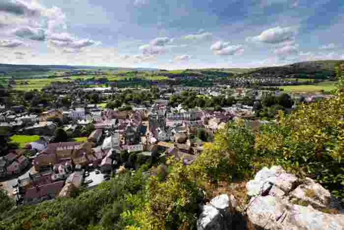 image Elevated view of a Yorkshire Dales market town with stone-roofed buildings, green fields, and rolling hills stretching into the distance.