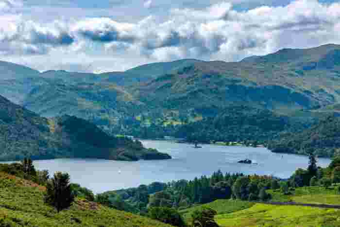 image Scenic view of Ullswater lake surrounded by green hills and mountains in the Lake District, with small sailboats on the water.