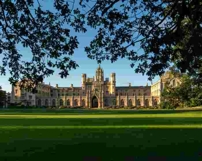 image St John's College at Cambridge University bathed in golden light, with its Gothic stone gateway framed by trees and a manicured lawn.