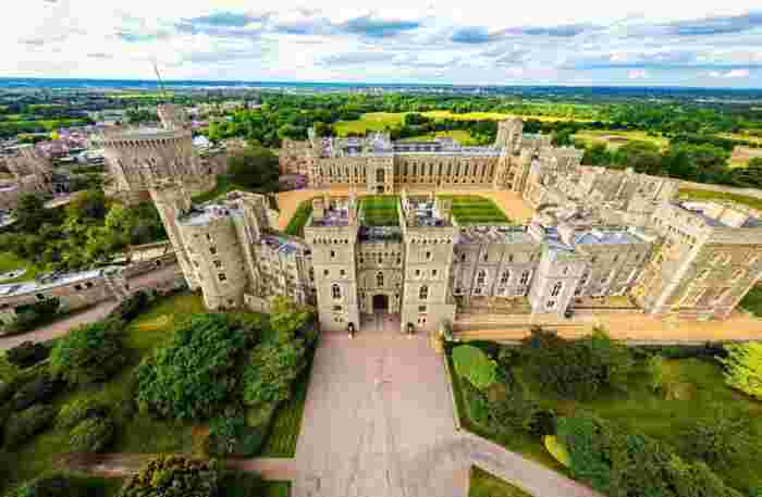image Aerial view of Windsor Castle's grand stone architecture surrounded by manicured gardens and green English countryside.