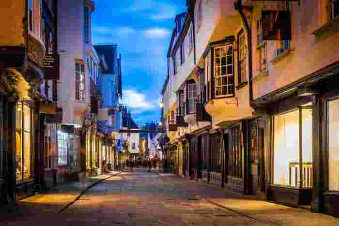 image The medieval cobbled street of the Shambles in York lit up at dusk, flanked by overhanging timber-framed buildings and glowing shop fronts.