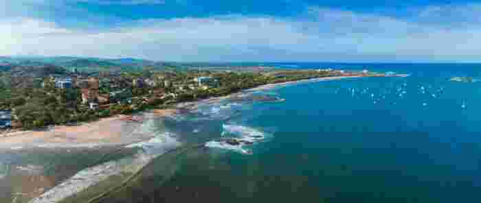 Aerial view of Guanacaste coastline with sandy beach, town, and boats in blue ocean