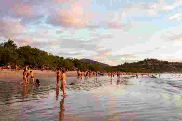 Busy tropical beach at sunset with people walking along the shoreline
