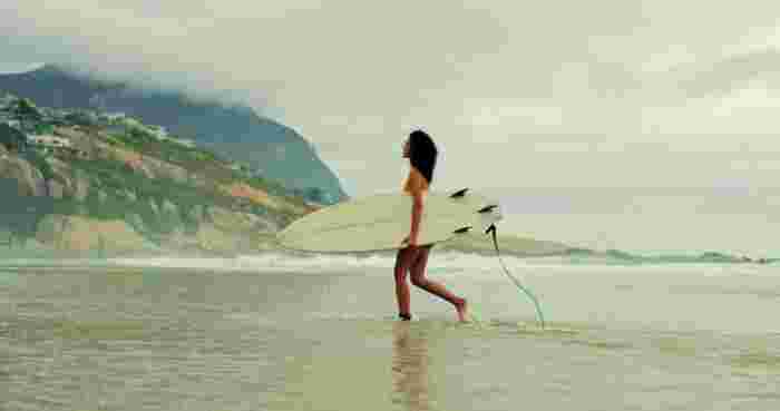 Surfer walking through shallow water with a surfboard along a misty beach coastline