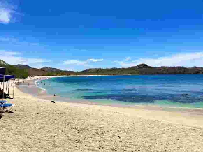Curved sandy bay in Costa Rica with clear blue water and people swimming under a bright sky