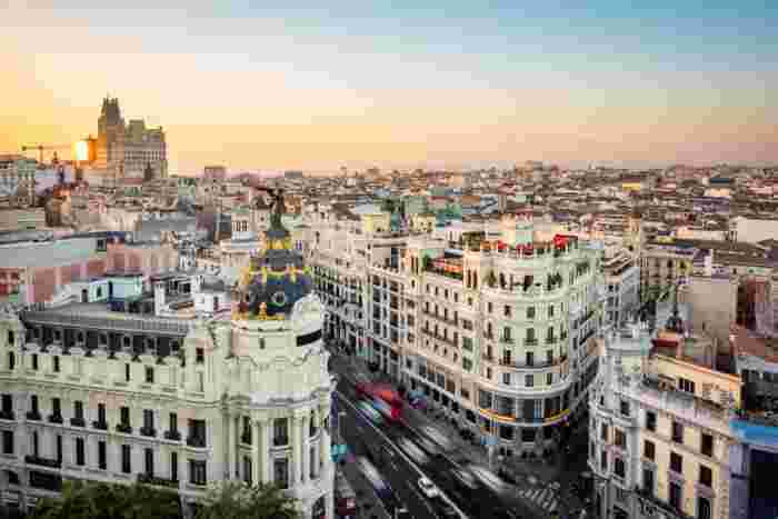 Aerial view of Madrid city center at sunset with Gran Vía traffic, historic architecture, and the Metropolis Building in the foreground.