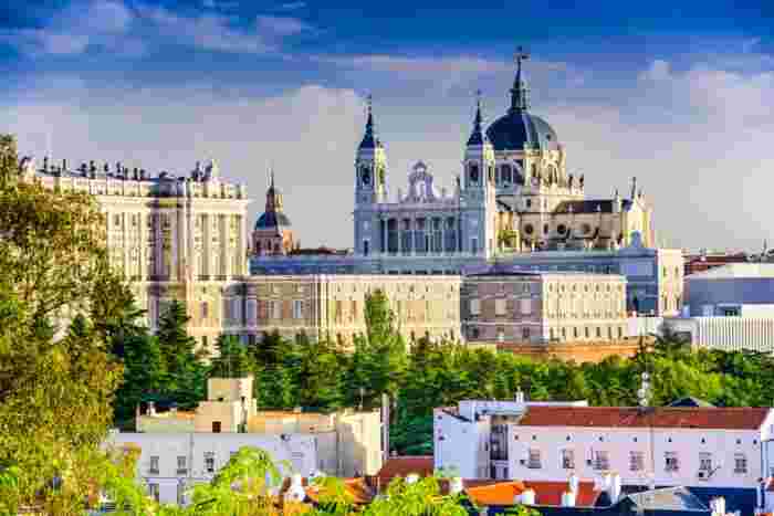 View of Almudena Cathedral and the Royal Palace in Madrid framed by trees and historic architecture. 