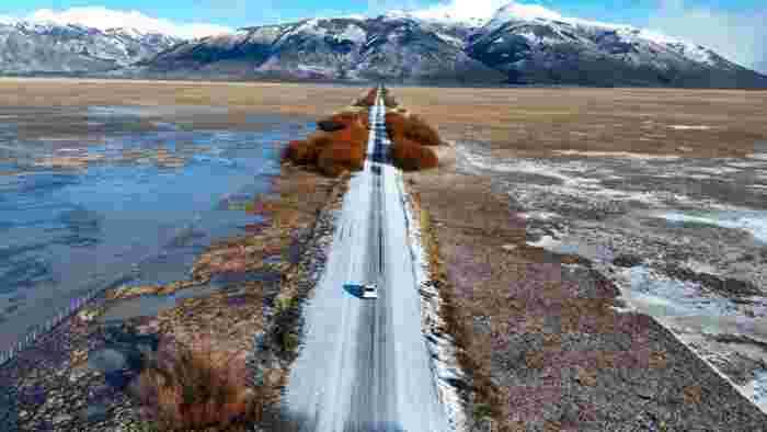 Winter road through Patagonian steppe with snow-covered Andes mountains in Argentina