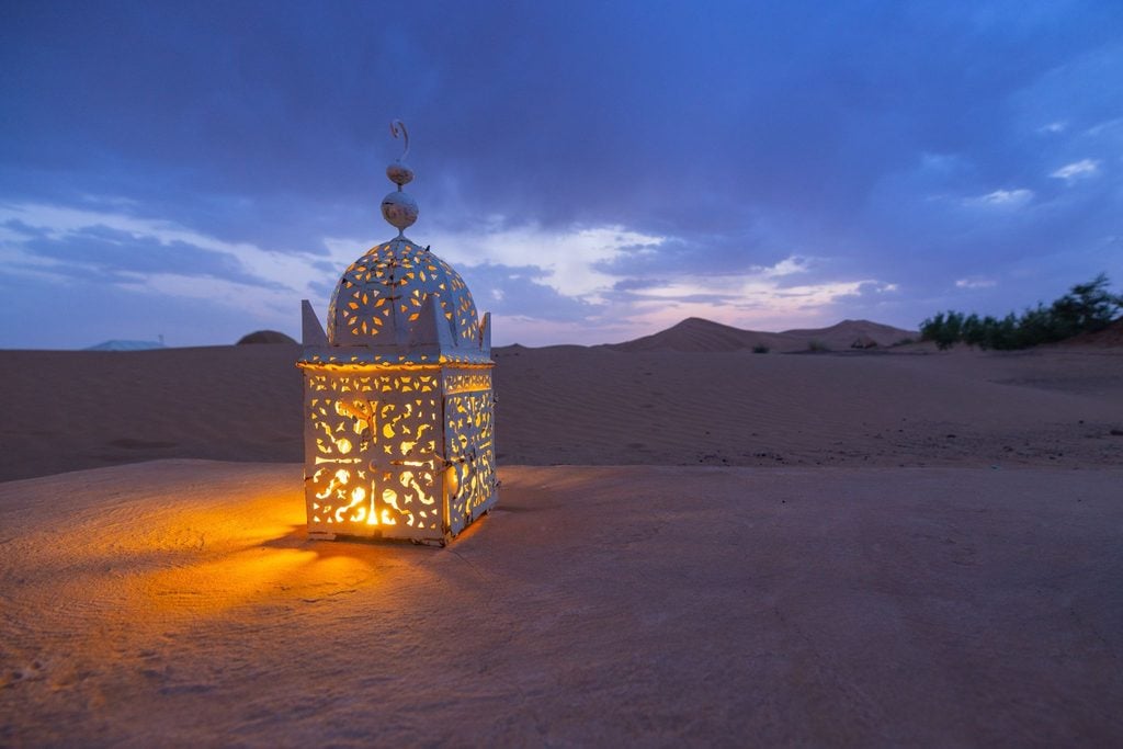 Glowing Moroccan lantern standing on a dune at dusk in the Sahara 