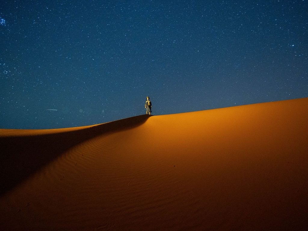 Person standing on a Sahara sand dune under a star-filled night sky 