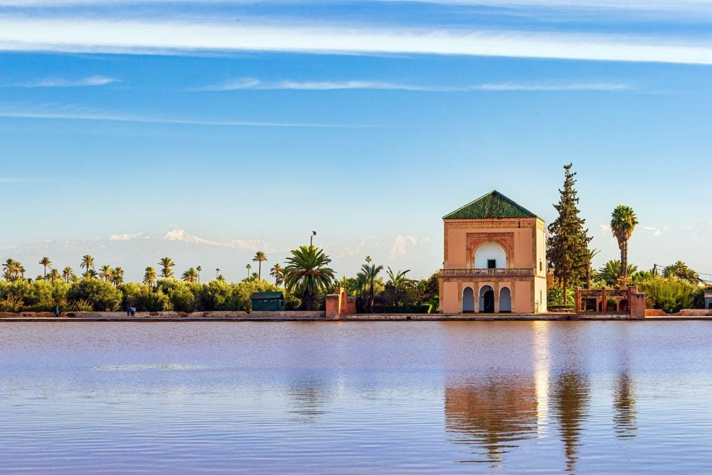 Reflection of a Marrakech pavilion and palm trees in a still garden pool 