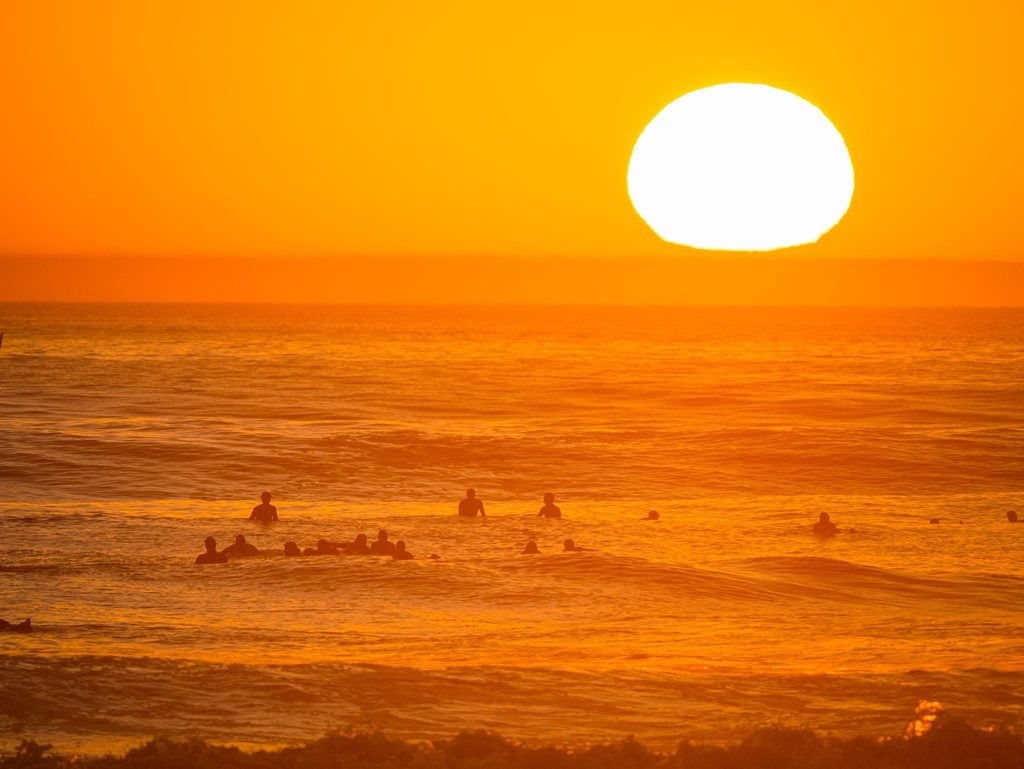 Surfers silhouetted in the ocean beneath a glowing orange sunset