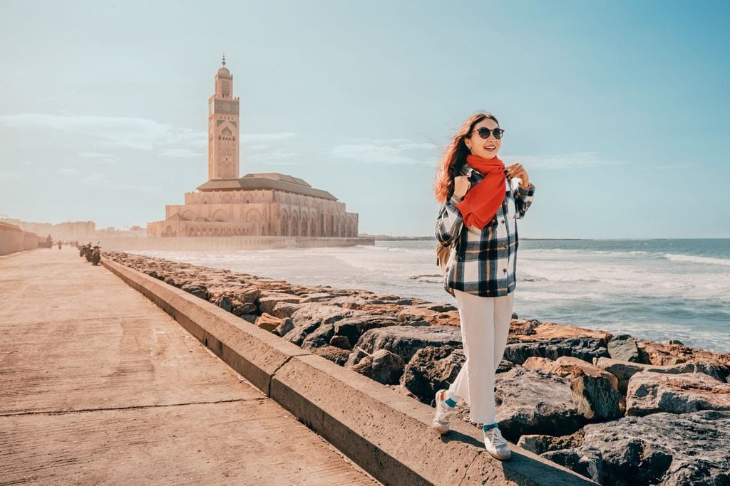 Traveler in a red scarf walking along the coast near the Hassan II Mosque