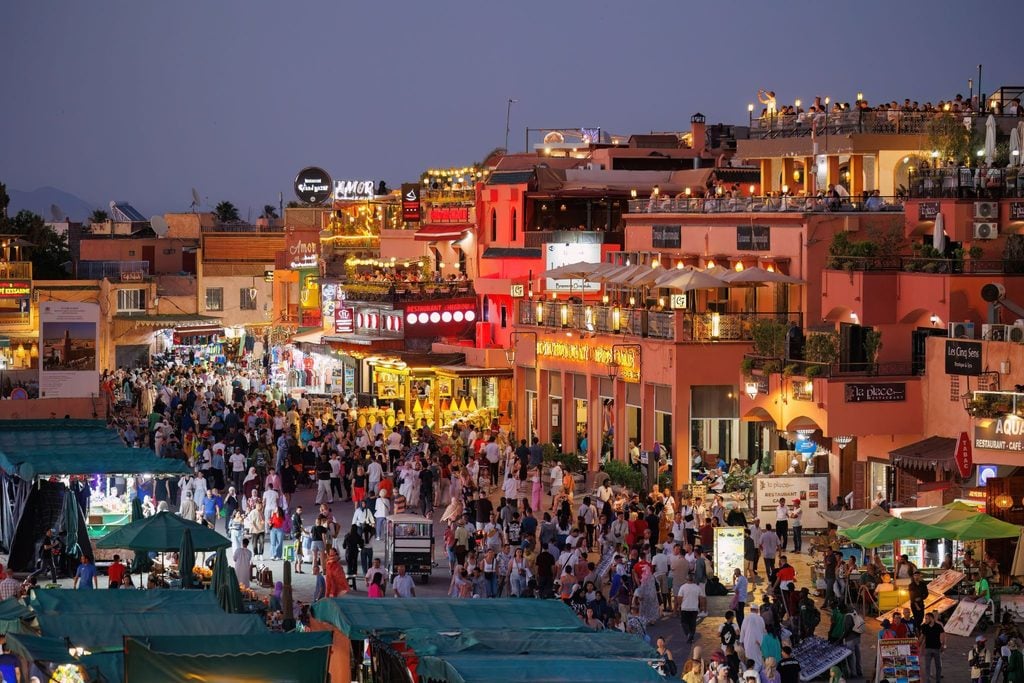 Crowded Marrakech square lit up with market stalls and restaurants at dusk 