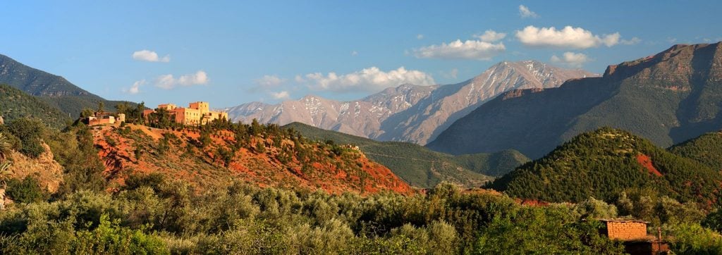 Kasbah-style villa on a red hillside beneath the snow-dusted Atlas Mountains 