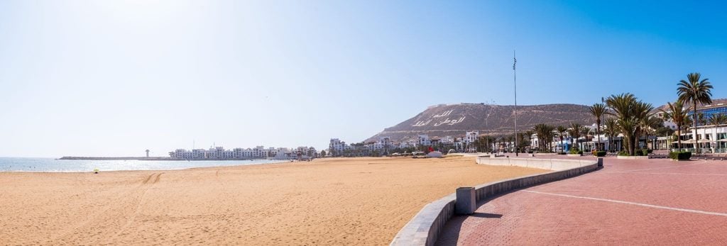 Empty sandy beach along Agadir's promenade with hills in the background 