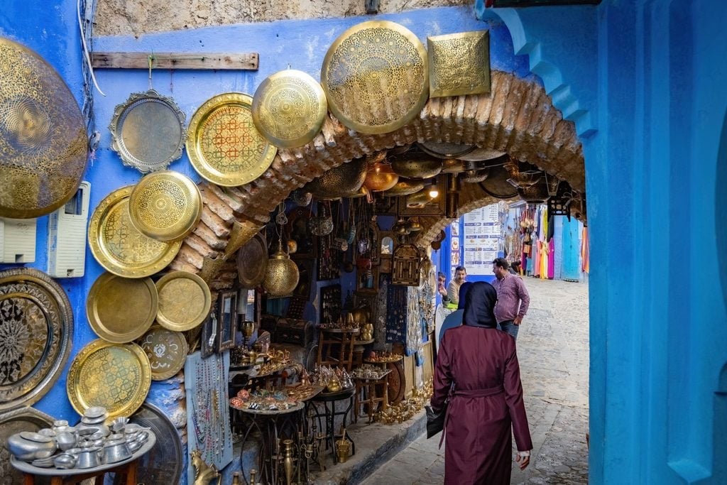 Golden brass plates and lanterns hanging in a blue-walled Chefchaouen market 