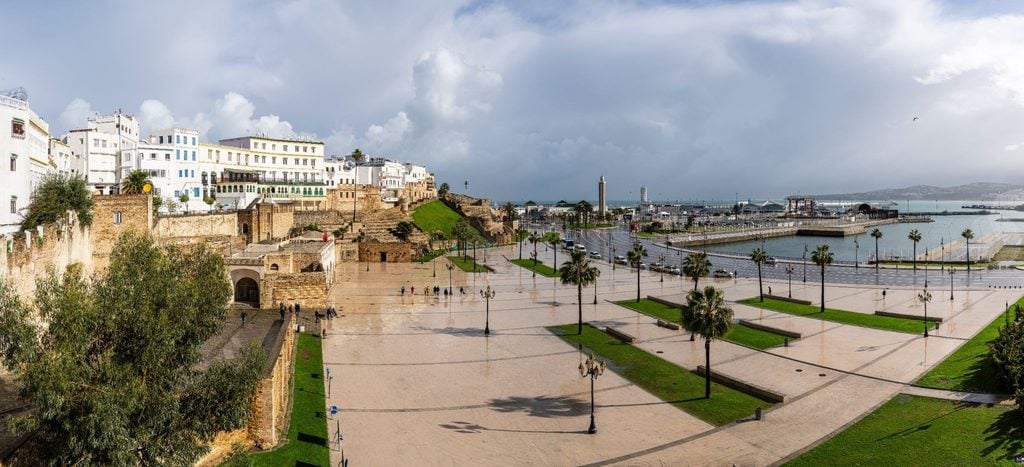 Panoramic view of a coastal Tangier plaza with palm trees and old kasbah walls 