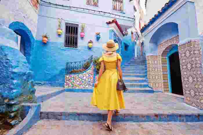 Woman in a yellow dress walking up blue stairs past a mosaic-tiled doorway in Chefchaouen's old town.