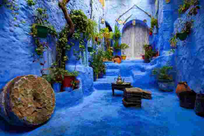 Vivid blue courtyard in Chefchaouen decorated with potted plants, a millstone, and a traditional tea set on a low table.