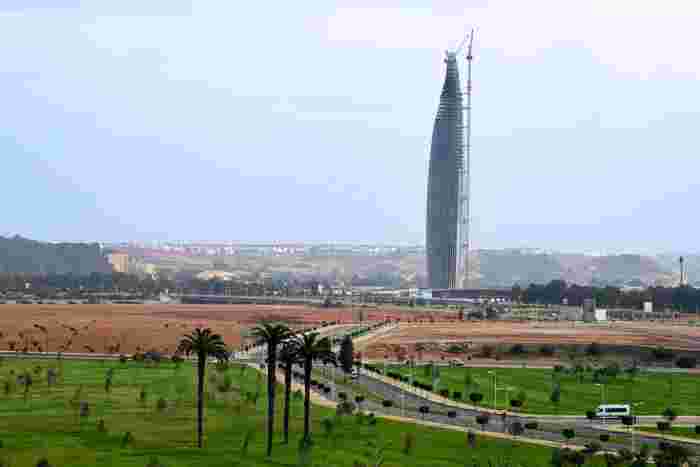 The Mohammed VI Tower under construction, rising above green parkland and palm-lined roads near Rabat.