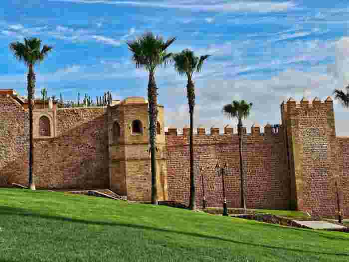 Rabat's historic stone ramparts, with an octagonal tower and crenellated walls behind palm trees and a green lawn.