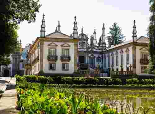 Baroque Mateus Palace in Vila Real with white facades, granite trim and ornate white pinnacles, seen across a garden pond with green plants in the foreground