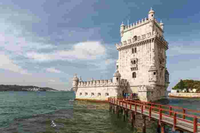 Belém Tower, a white limestone fortress with Manueline carvings on the bank of the Tagus River in Lisbon, with a red wooden walkway leading to its entrance