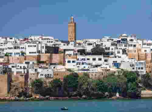 The whitewashed houses and stone minaret of the Kasbah of the Udayas, seen across the Bou Regreg River with a small rowboat in front.
