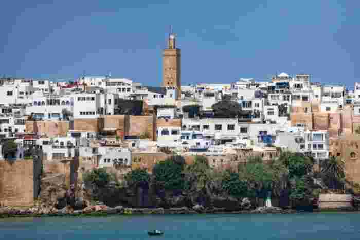 The whitewashed houses and stone minaret of the Kasbah of the Udayas, seen across the Bou Regreg River with a small rowboat in front.